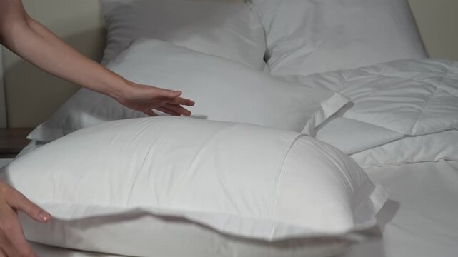 white pillows on the bed, female hands rearranging the bedclothes