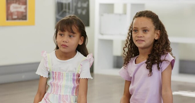 Diverse female children sitting in class after teacher cue by cubby while right child raising hand