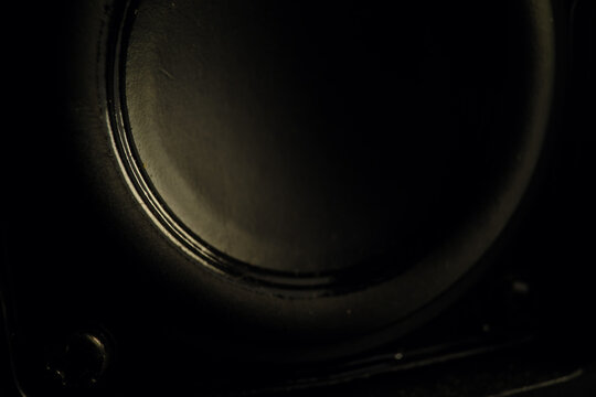 Dark macro shot of a black speaker cone in low light. Close-up texture of audio equipment emphasizing the circular woofer shape and modern sound technology.