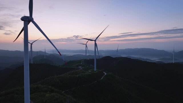 Wind turbines silhouetted against sunset sky in mountainous wind farm landscape