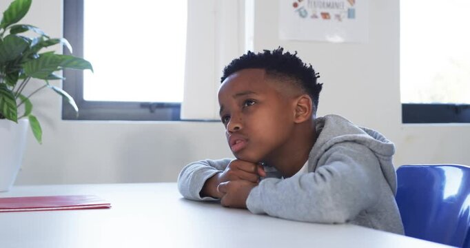 African male youth student watching off-camera voice at school table, making head turns holding pen