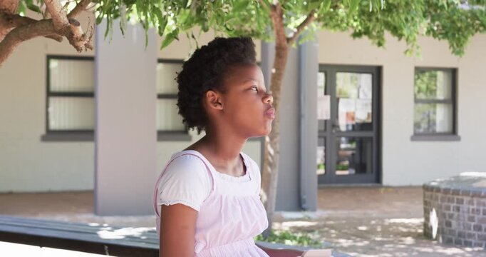 African American girl sitting in courtyard on bench under tree looking up grabbing snack from box