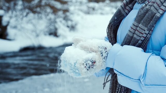 Women's hands in warm knitted mittens hold clean and crumbly white snow. Winter in the northern area. People in winter.