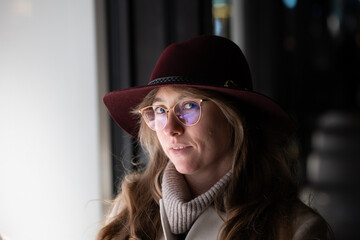 Young Caucasian woman wearing a hat and winter clothing smiling at the camera next to a shop window at night. Close up night portrait, shallow depth of field