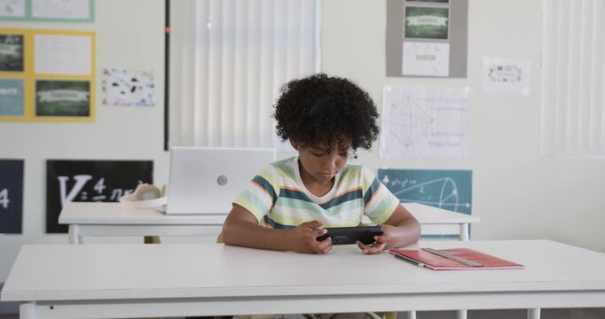 African American teen male tapping handheld device, following cues in class with red folder right