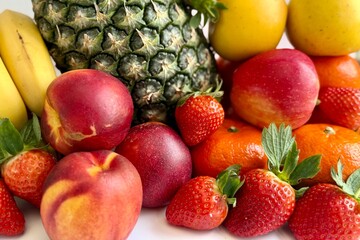 Assorted fresh fruits including pineapple, bananas, peaches, strawberries, and oranges arranged together, colorful healthy food selection showing natural freshness and variety.