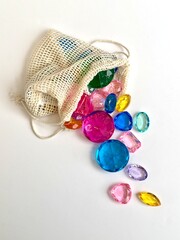 Colorful decorative gemstones spilling from a reusable cotton mesh bag on a white background. Concept image representing sustainability, eco friendly lifestyle, zero waste shopping, creativity