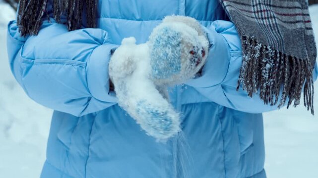 Women's hands in warm knitted mittens hold clean and crumbly white snow. Winter in the northern area. People in winter.