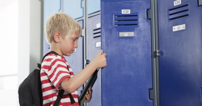 Male child student arriving at blue lockers beside bright window, opening C32 and storing tablet