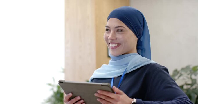 Woman staff wearing navy scarf and badge holding tablet in lobby reacting to offscreen cue smiling