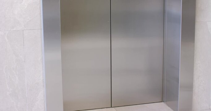 Steel elevator doors are opening, revealing nurse with tablet and speaking to colleague in lobby