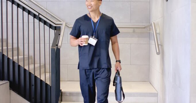 Diverse staff in scrubs descending stairs, man smiling, colleagues joining with IDs holding coffee