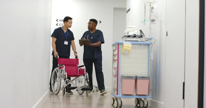 Diverse male staff consulting tablet after colleague arriving with pink wheelchair, planning scans