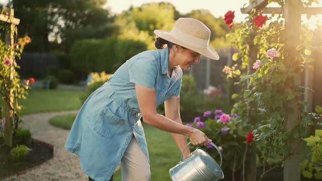 Joyful happy amputee woman with prosthetic leg embracing her outdoor hobby, watering lush garden with her faithful dog for truly peaceful and content lifestyle