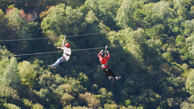Ziplining. Two women slide down a steel cable over a gorge. One of them is filming.