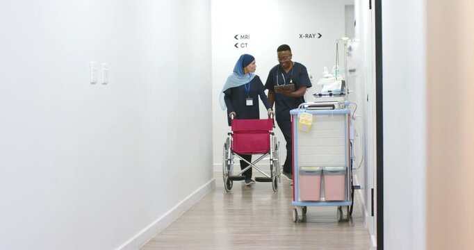 Diverse coworkers, male entering with tablet, female in headscarf pushing pink wheelchair to MRI