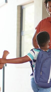 Vertical video: Raising hand striped polo son rust top mom high-fiving at door navy pack to school