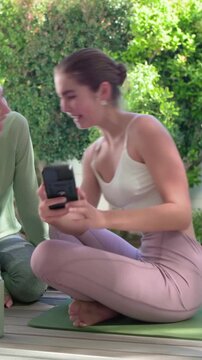 Vertical video: Leaning woman in white crop top and pink tights showing camera print to pal on deck