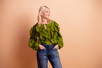 A mature beautiful female woman with blonde hair wearing a green blouse and jeans stands...