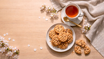 Tea and cookies flat lay with soft spring petals on textured linen. Airy seasonal tea time background with elegant styling and generous copy space ideal for lifestyle and editorial designs.
