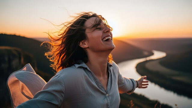 Woman laughing with arms outstretched at sunset by a river