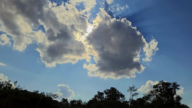 A hyperlapse scene of two large, fluffy clouds spectacularly merging, like butter melting. Brilliant sunbeams burst through the gaps, illuminating the blue sky in a stunning display of nature's power.
