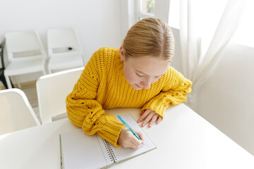 Teenage girl writing in notebook at white table, focused student studying at home, education concept, homework process, learning routine
