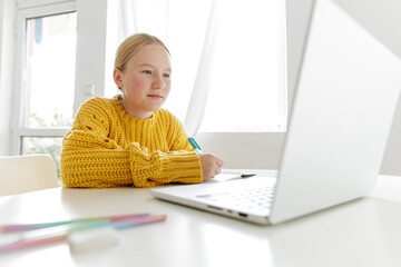 Teenage girl studying online at home, focused student writing in notebook with laptop, distance learning, homeschooling concept, education and technology