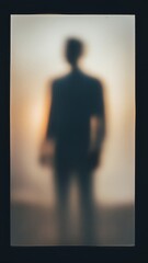 Fototapeta premium Blurry dark silhouette of a mysterious person standing behind frosted glass with a warm glowing backlight creating a moody and anonymous atmosphere