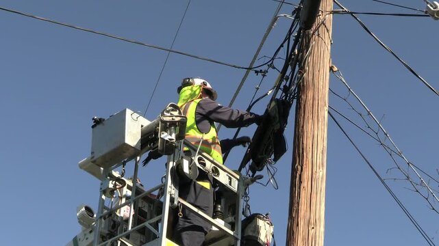 Telephone repair technician checks cable bundle for customer connectivity problem, in lift basket.  No logo, no recognizable visage.