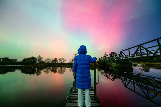 Magische bunte Nordlichter mit Spiegelung &uuml;ber Wasser und Steg mit Frau im Winter