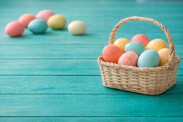 Pastel Easter eggs in wicker basket on turquoise wooden background with copy space
