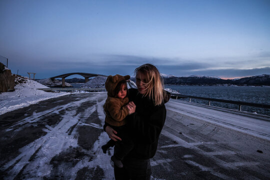 Mujer cagando a su hija en Atlantic Ocean road. Mother holding her daughter on Atlantic Ocean Road in winter, Norway. Mother and daughter exploring Atlantic Ocean Road in Norway during winter