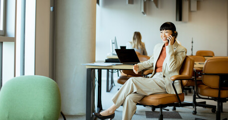 Businesswoman talking on a phone in a modern office workspace in the afternoon
