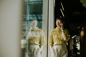 Happy woman talking on phone while standing by window in modern cafe interior