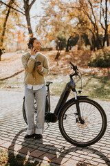 Cheerful woman enjoys an autumn day while talking on the phone near her bicycle