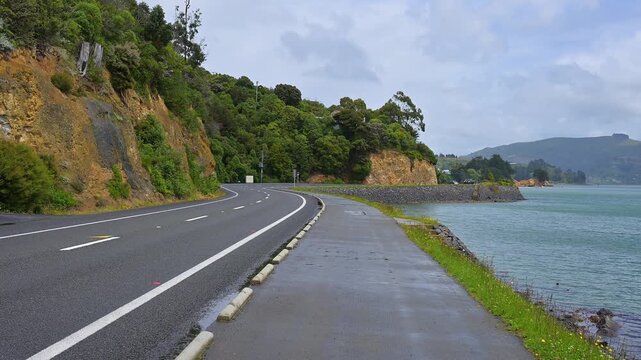 K&uuml;stenstra&szlig;e entlang des Wassers mit B&auml;umen und Felsen im Hintergrund, Broad Bay, Dunedin, Otago, S&uuml;dinsel, Neuseeland, Ozeanien 