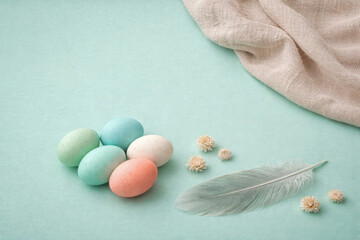Pastel Easter eggs with feather and dried flowers on mint blue background copy space