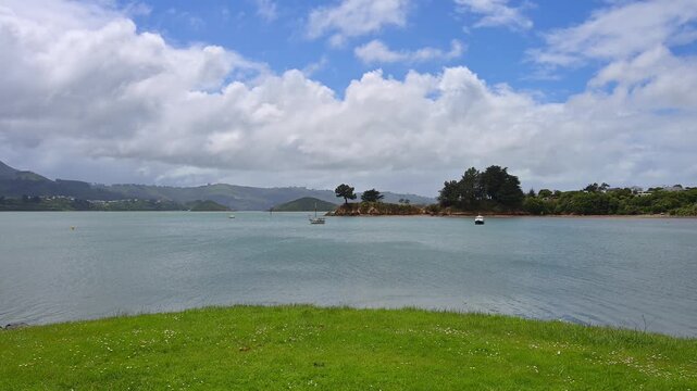 Blick von einer Wiese auf das Meer unter einem blauen Himmel voller Wolken, Broad Bay, Dunedin, Otago, S&uuml;dinsel, Neuseeland, Ozeanien