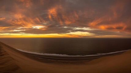 Serene beach scene at sunset with vibrant orange clouds and calm ocean waters meeting the sandy shore with gentle waves