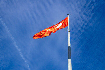 National flag of Turkey with white crescent and star waving on a flagpole against a vibrant blue sky with light clouds. Patriotic symbol of the Turkish Republic. October, Antalya, Turkey.