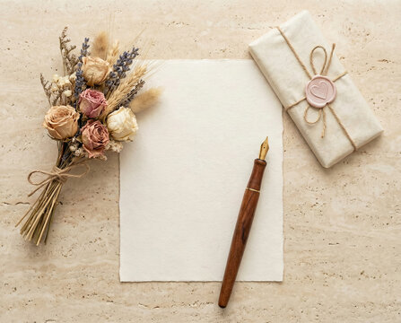 flat lay vista desde arriba sobre una superficie neutra  una hoja de papel, una lapicera  un peque&ntilde;o ramo de flores y un chocolate envuelto con sello de corazon