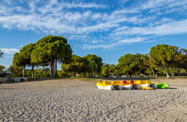 Rows of colorful paddle boats and kayaks on the pebble shore of Konyaalti beach. Green trees and altocumulus ripple clouds on a blue sky. October, Antalya, Mediterranean region, Turkey.