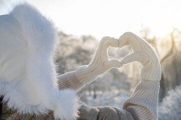 Woman in fur coat making heart shape with hands in snowy park, winter love concept
