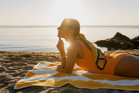 beautiful blond smiling woman lying on beach tanning sunbathing on summer season vacation wearing yellow swimsuit, stylish accessories