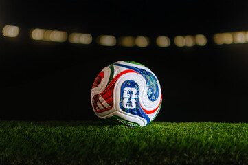 Obraz premium FIFA World Cup 2026 themed background with official black edit space and orange stadium bokeh lights, official Trionda ball on green grass