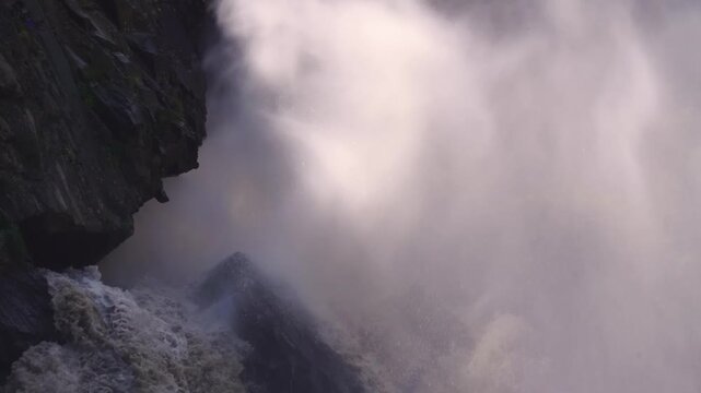 Footage of a fast-flowing waterfall in the rugged landscape of Dagestan, a republic in the North Caucasus region of Russia. The water creates significant mist and spray as it crashes down near dark ro