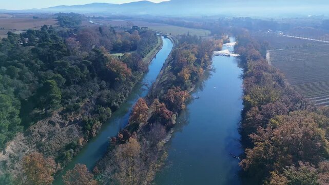 Aerial flyover of a canal and river flowing parallel through autumn forest, sunny day 4K drone
