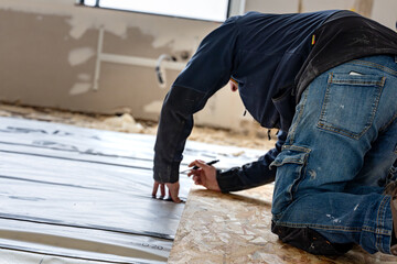 Artisan en train de mesurer et tracer des rep&egrave;res sur des panneaux lors de travaux de r&eacute;novation int&eacute;rieure, illustrant la pr&eacute;cision du chantier et la pr&eacute;paration de la pose.