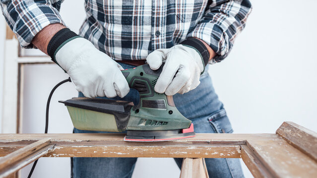 Craftsman. Adult carpenter using an electric sander to smooth an old wooden window. Construction industry, carpentry, housework do it yourself, moving sanding plate. Workplace safety. Restoration.